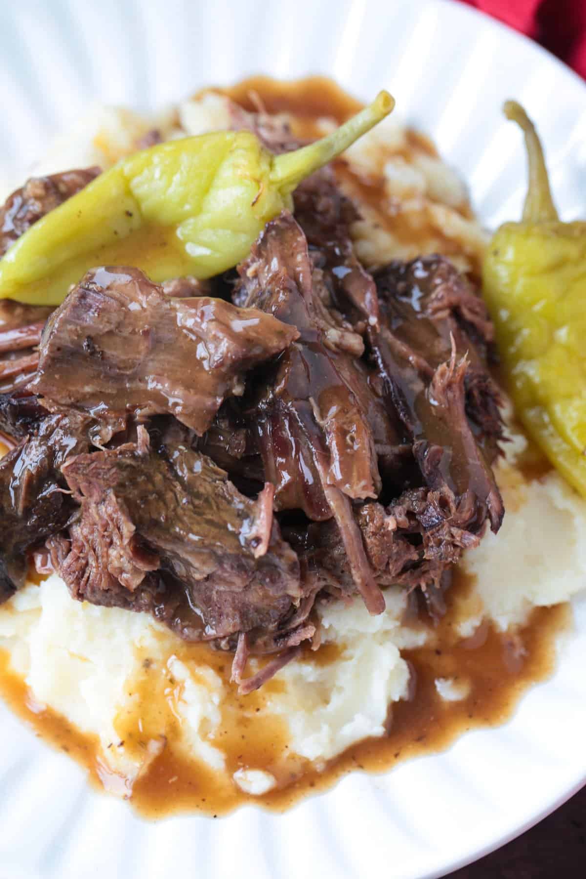 Slow Cooker Mississippi Pot Roast is tender and delicious in a tangy brown gravy. An easy crock pot dinner the whole family will love! mississippi pot roast on bed of mashed potatoes with gravy