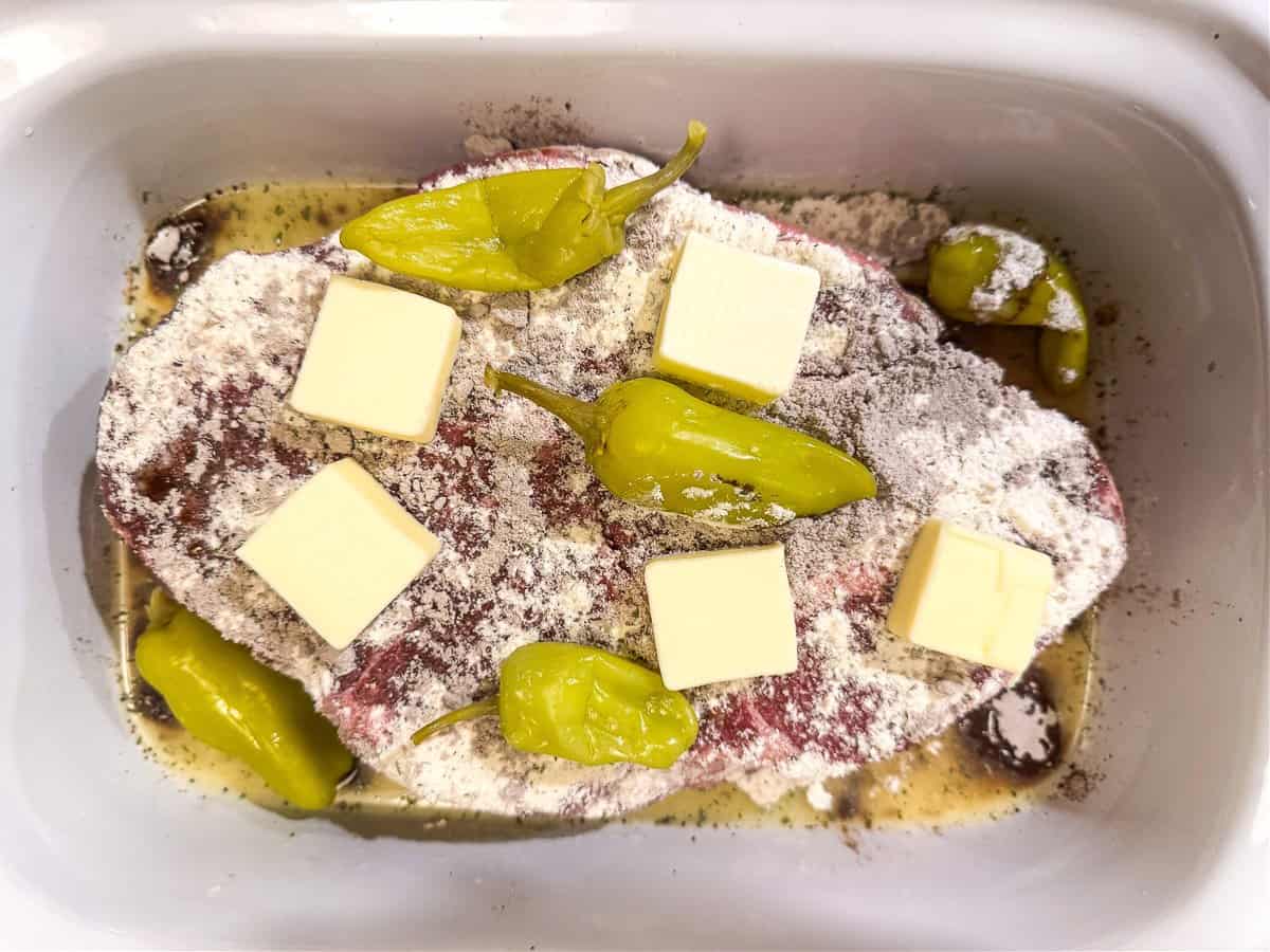 Slow Cooker Mississippi Pot Roast is tender and delicious in a tangy brown gravy. An easy crock pot dinner the whole family will love! chuck roast in slow cooker with peppers and butter