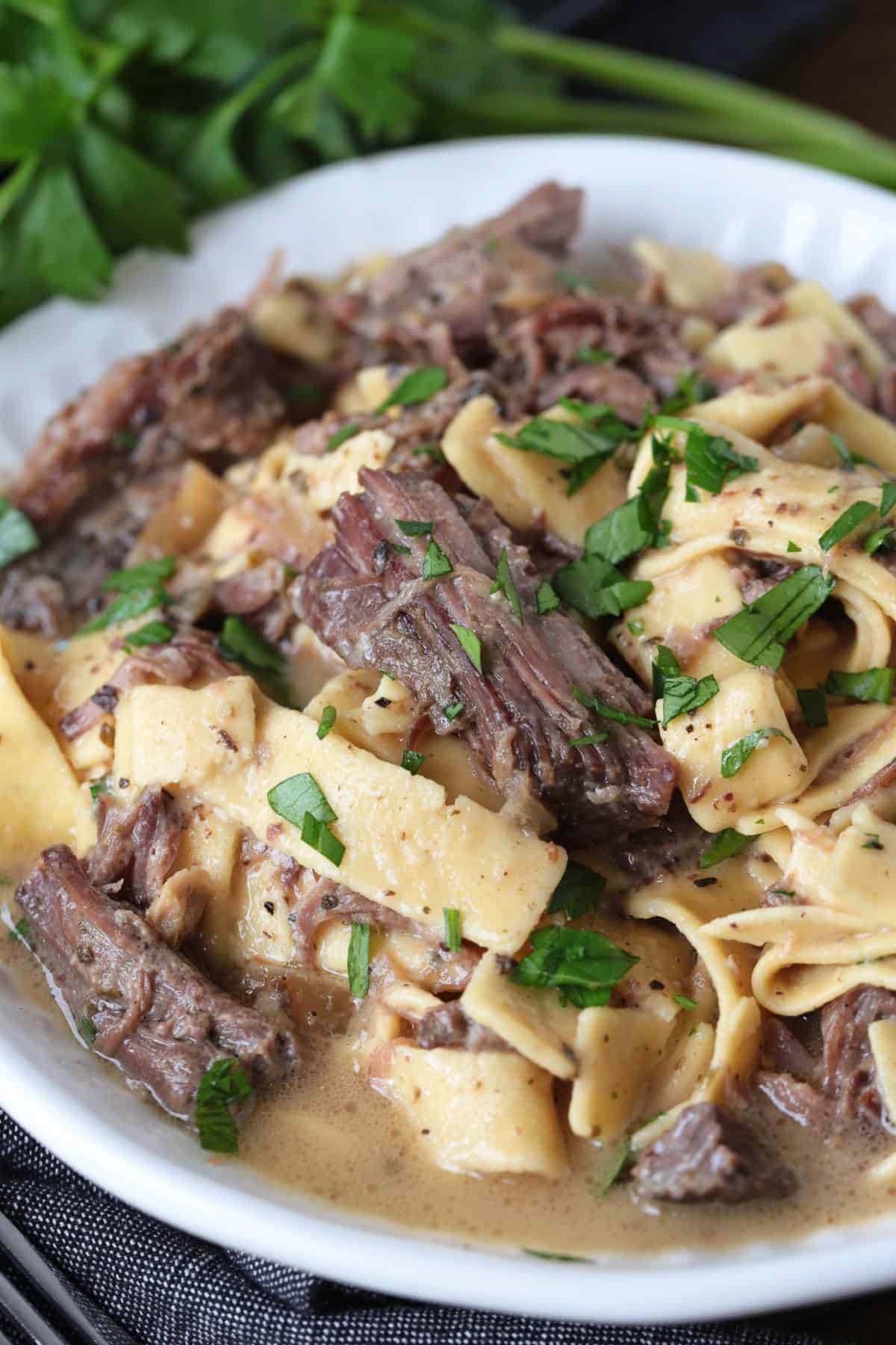 beef and noodles in a bowl with fresh parsley on top