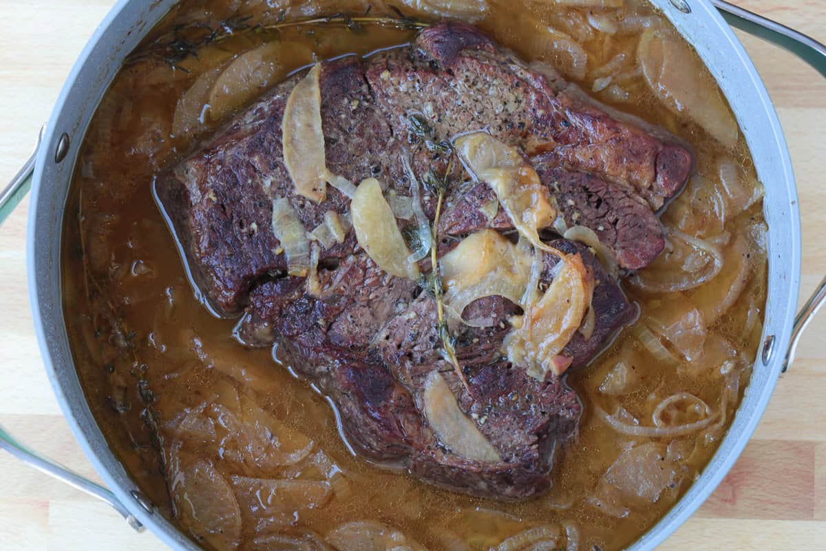 seared pot roast in pot with apples, onions, apple cider and beef broth