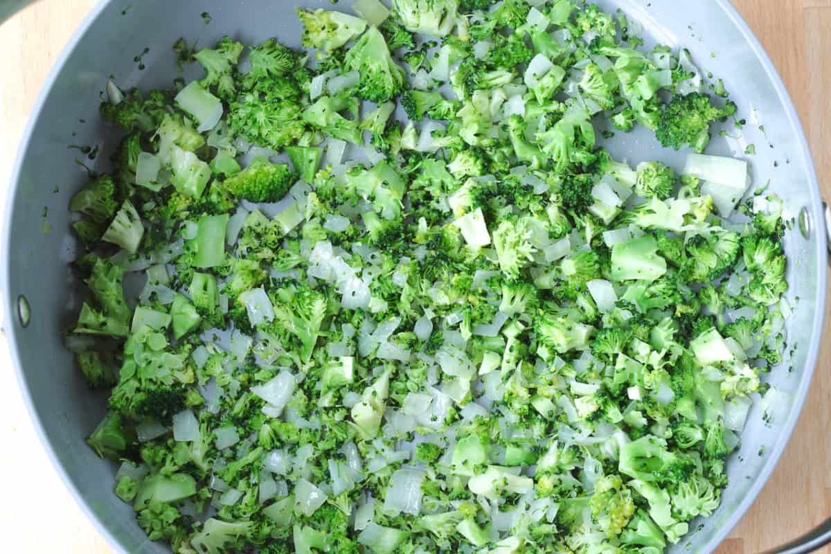 This Cheesy Broccoli Orzo is the ultimate comfort food side dish! Perfect alongside chicken or steak, or on its own for an easy, cozy dinner. chopped onions and broccoli in a pot