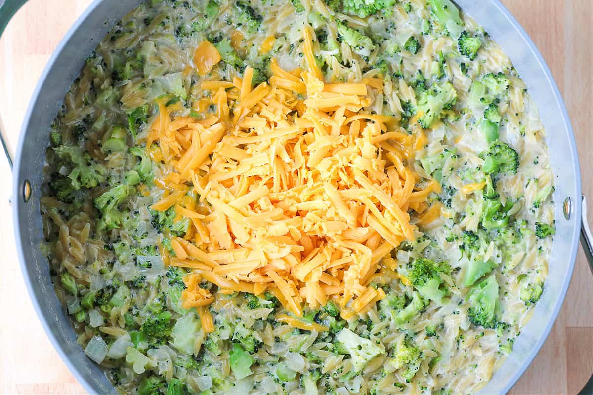 This Cheesy Broccoli Orzo is the ultimate comfort food side dish! Perfect alongside chicken or steak, or on its own for an easy, cozy dinner. shredded cheddar cheese in a pot with creamy broccoli orzo