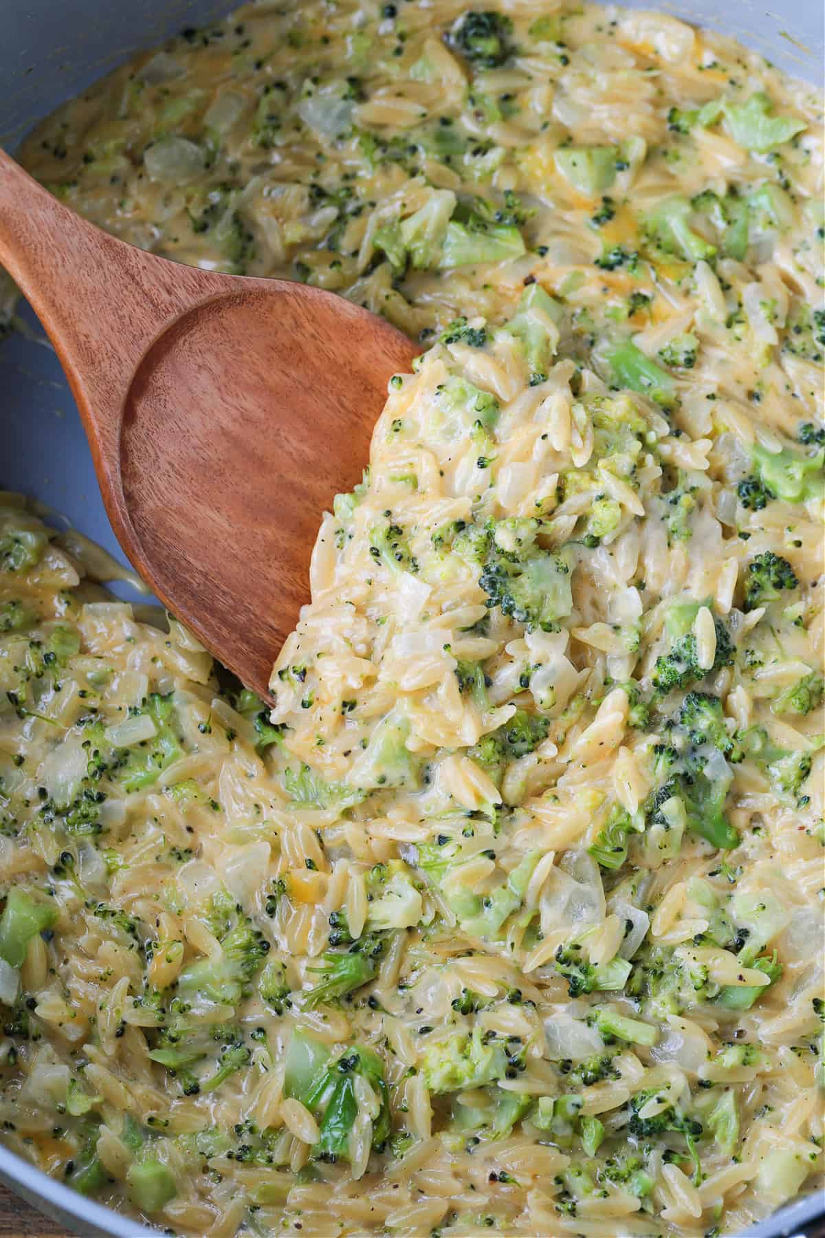 This Cheesy Broccoli Orzo is the ultimate comfort food side dish! Perfect alongside chicken or steak, or on its own for an easy, cozy dinner. broccoli and cheese orzo in a pot with a wooden serving spoon