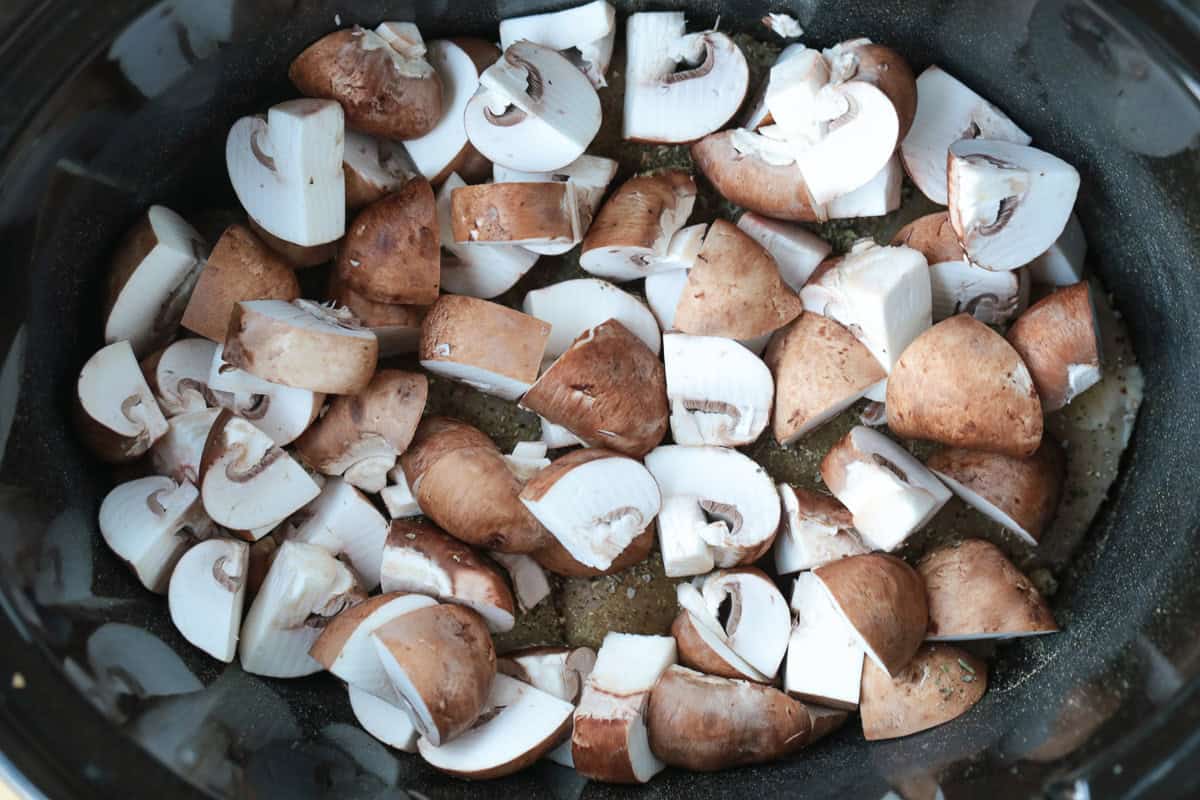 This cozy Slow Cooker Chicken Stroganoff is creamy and hearty, we love it for busy weeknights or lazy weekends. An easy comfort food dinner! chopped mushrooms in a slow cooker over chicken breasts