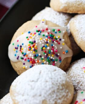 italian wedding cookies with powdered sugar and sprinkles on black platter