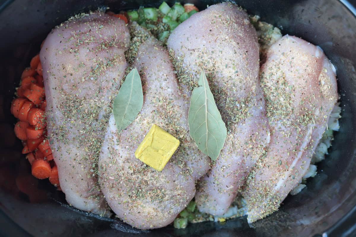 seasoned chicken breasts in a slow cooker with bay leaves and chicken bouillon cube