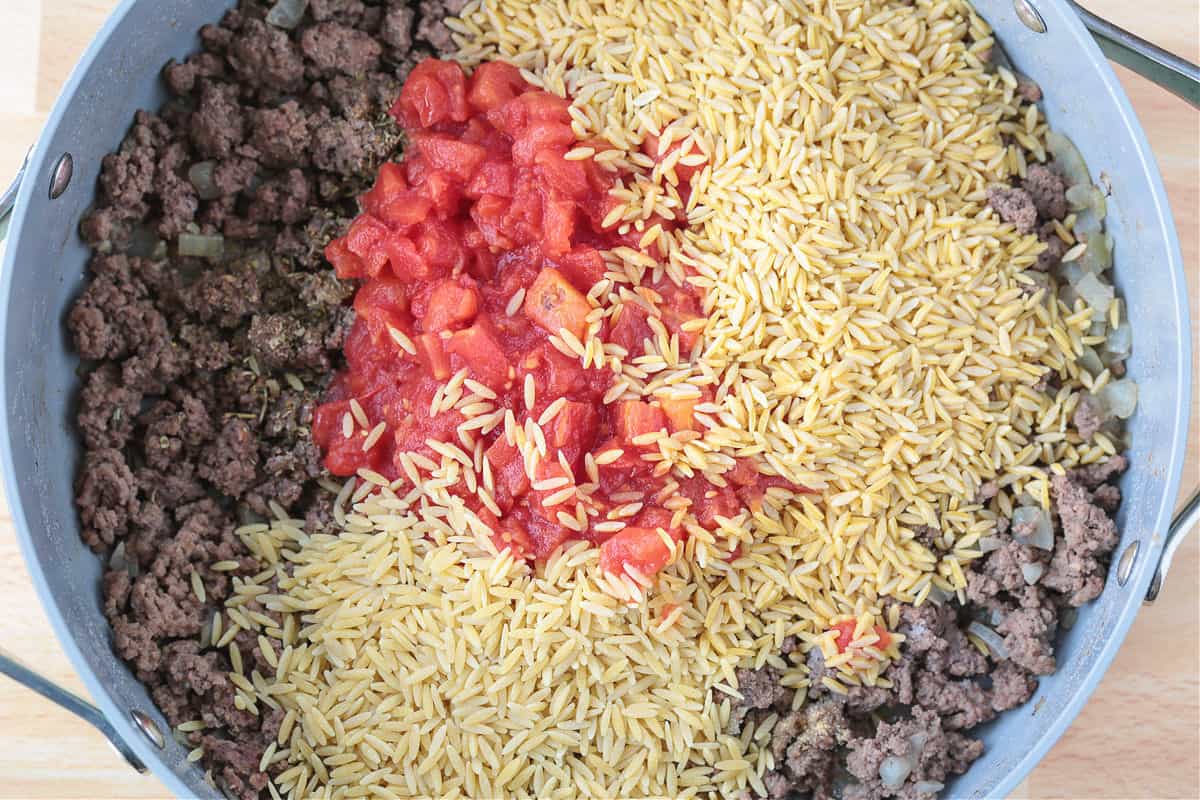 Spinach and Beef Orzo is a comfort food meal that's done in 30 minutes! Tender orzo with ground beef and spinach in a cheesy, creamy sauce. a deep skillet with ground beef, diced tomatoes and orzo