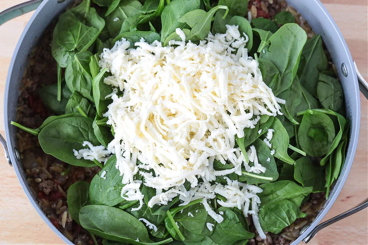 Spinach and Beef Orzo is a comfort food meal that's done in 30 minutes! Tender orzo with ground beef and spinach in a cheesy, creamy sauce. fresh spinach and mozzarella cheese in a skillet with ground beef and orzo