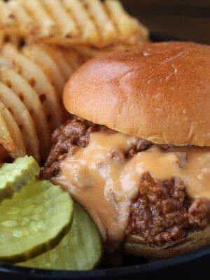 close up of cheesy sloppy joe on black plate with pickles and waffle fries
