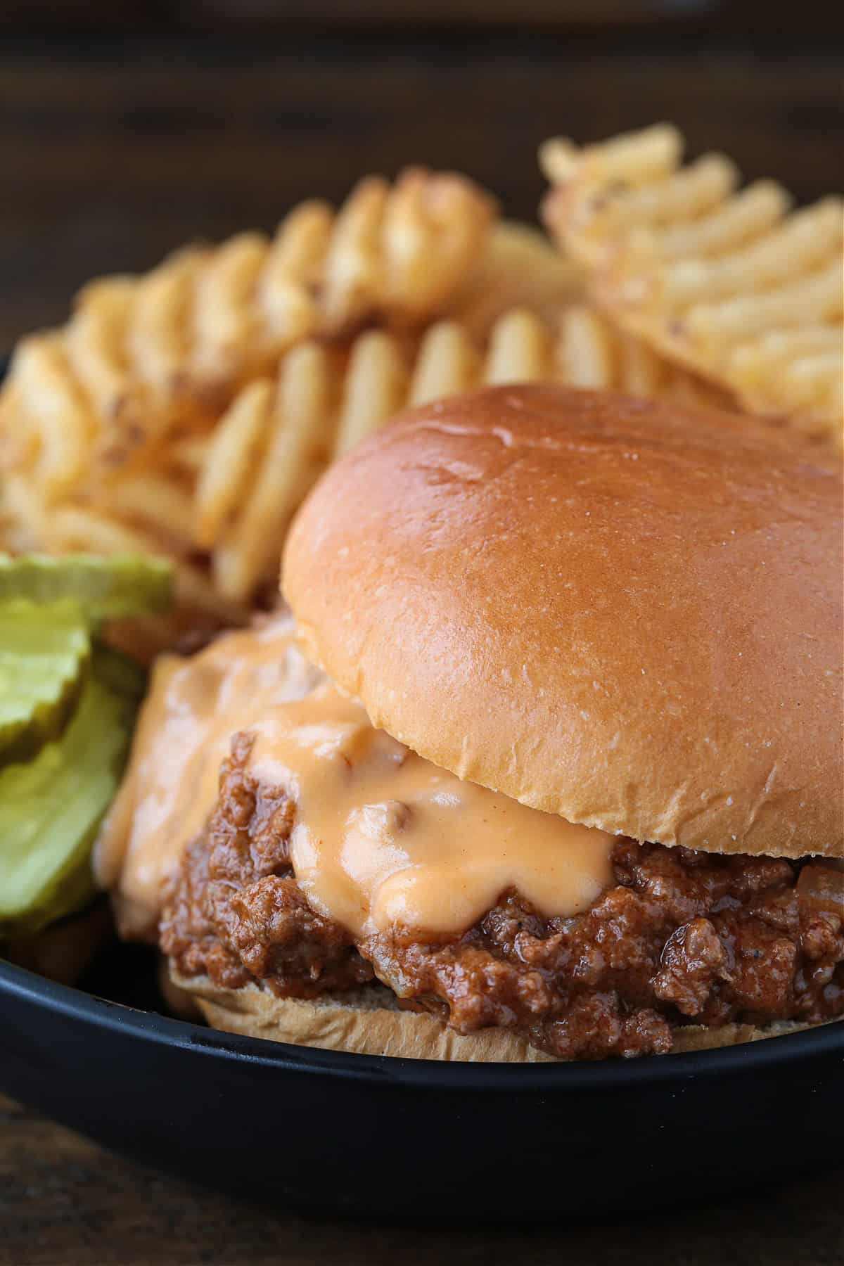 sloppy joe with cheese on black plate with waffle fries and pickles