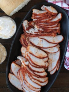 sliced turkey on a black platter with condiments on the side