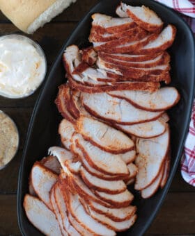 sliced turkey on a black platter with condiments on the side