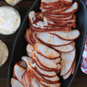 sliced turkey on a black platter with condiments on the side