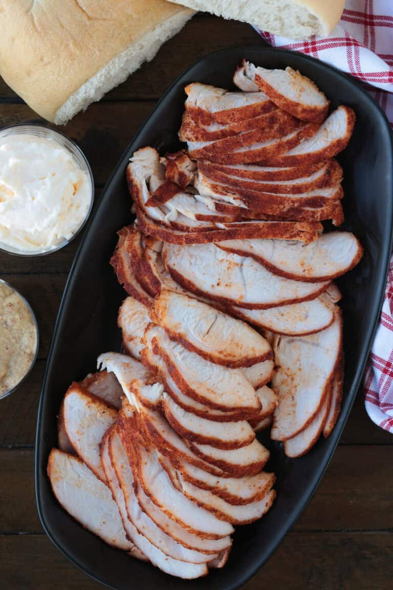 sliced turkey on a black platter with condiments on the side