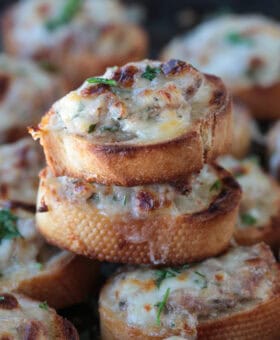 cheesy sausage crostini stacked on a tray of crostini
