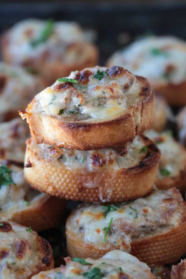cheesy sausage crostini stacked on a tray of crostini