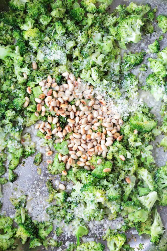 chopped broccoli in a skillet with pine nuts and parmesan cheese