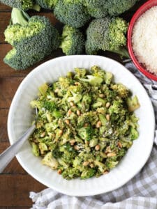 shaved broccoli in a white bowl with pignoli nuts and parmesan cheese