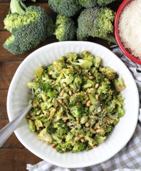 shaved broccoli in a white bowl with pignoli nuts and parmesan cheese