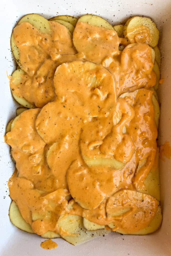 sliced potatoes in a casserole dish with cheese sauce