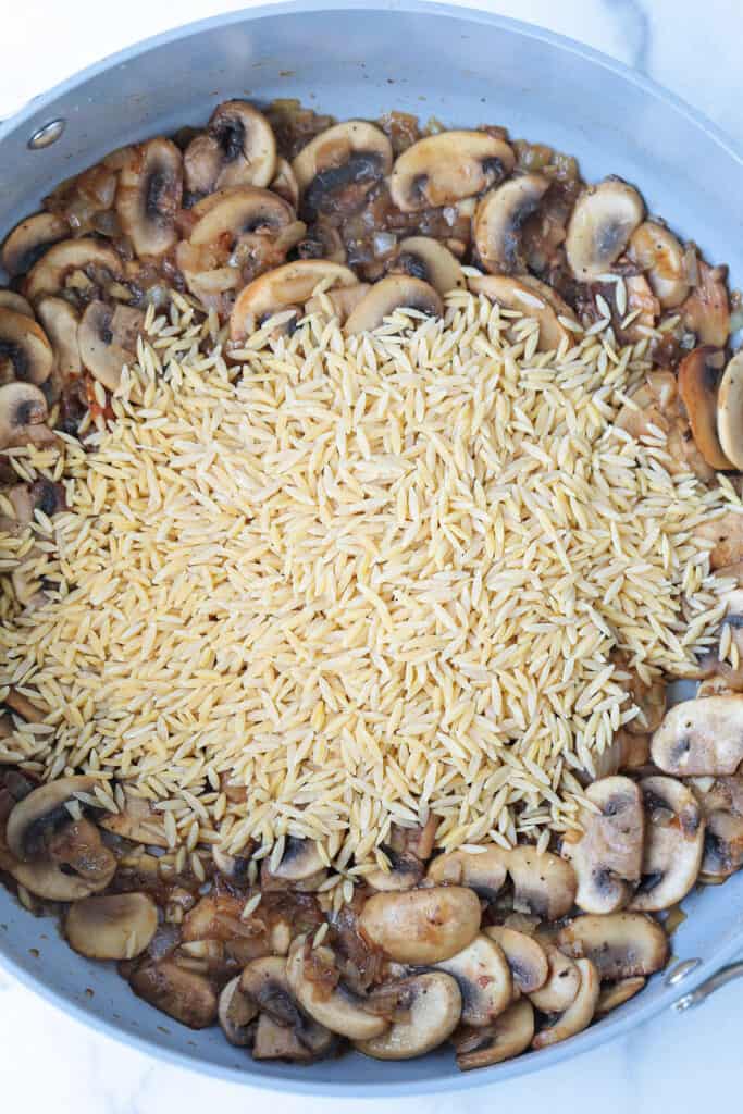 mushrooms in skillet with uncooked orzo
