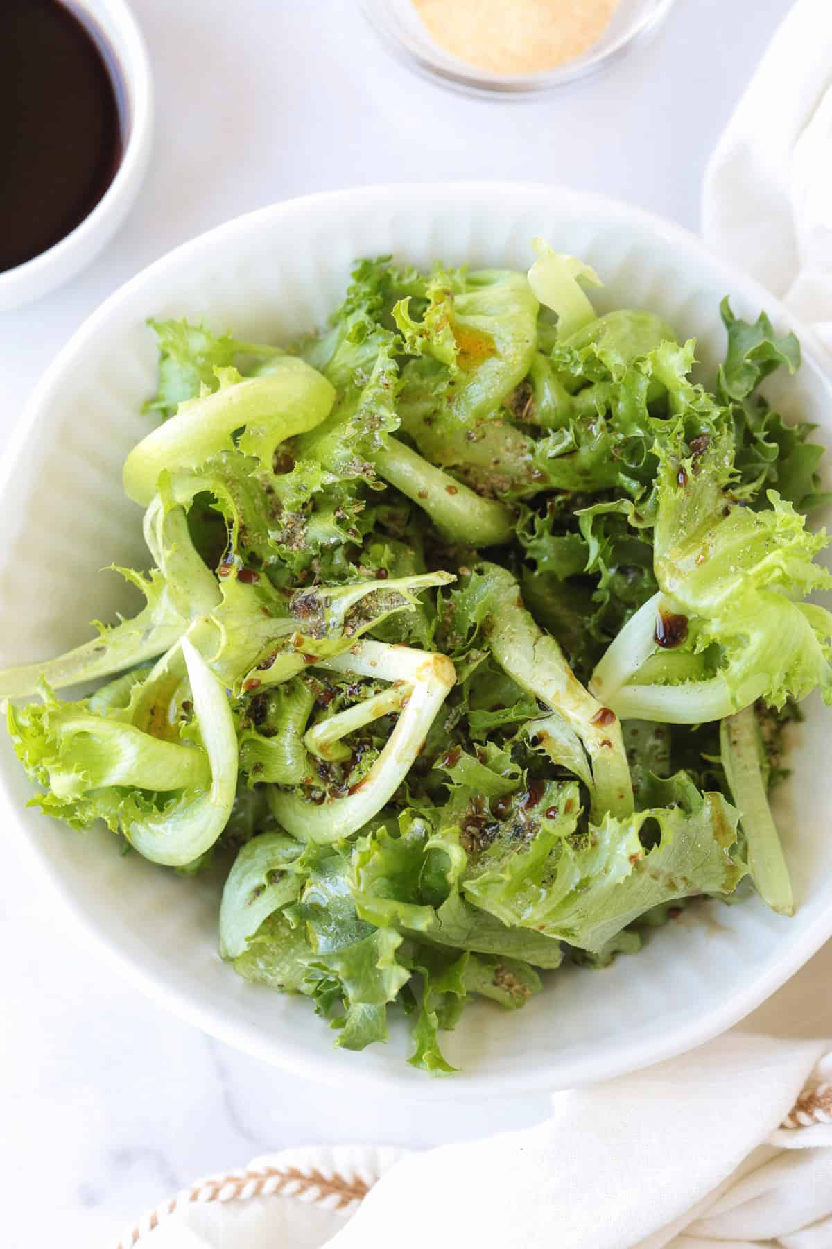 lettuce in a bowl with seasonings and balsamic vinegar