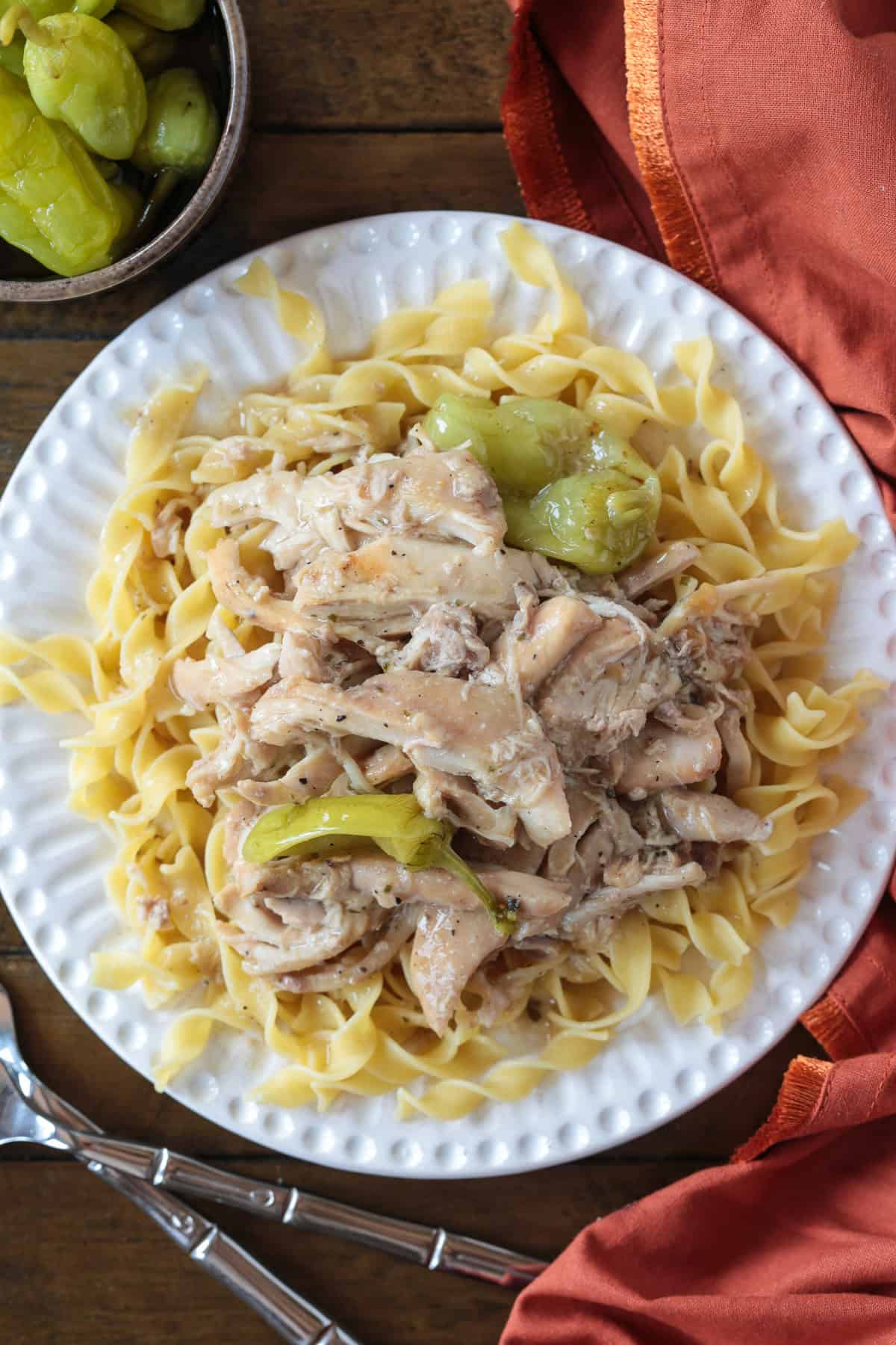 Mississippi Chicken is an easy, 5 ingredient dinner! Tender chicken in a tangy and zesty gravy spooned over mashed potatoes or noodles! shredded chicken with peppers over egg noodles on white plate