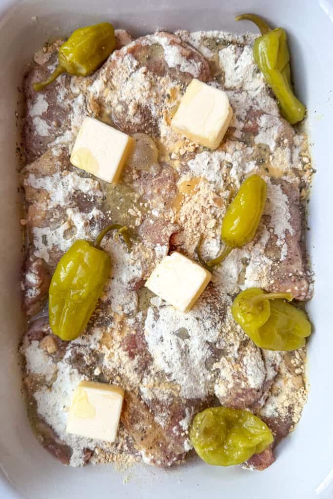 Mississippi Chicken is an easy, 5 ingredient dinner! Tender chicken in a tangy and zesty gravy spooned over mashed potatoes or noodles! chicken in a slow cooker with peppers, seasonings and butter