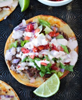 smash taco with toppings and sauce and limes on the side