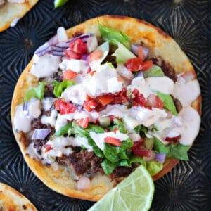 smash taco with toppings and sauce and limes on the side