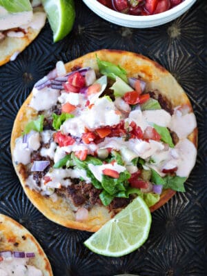 smash taco with toppings and sauce and limes on the side
