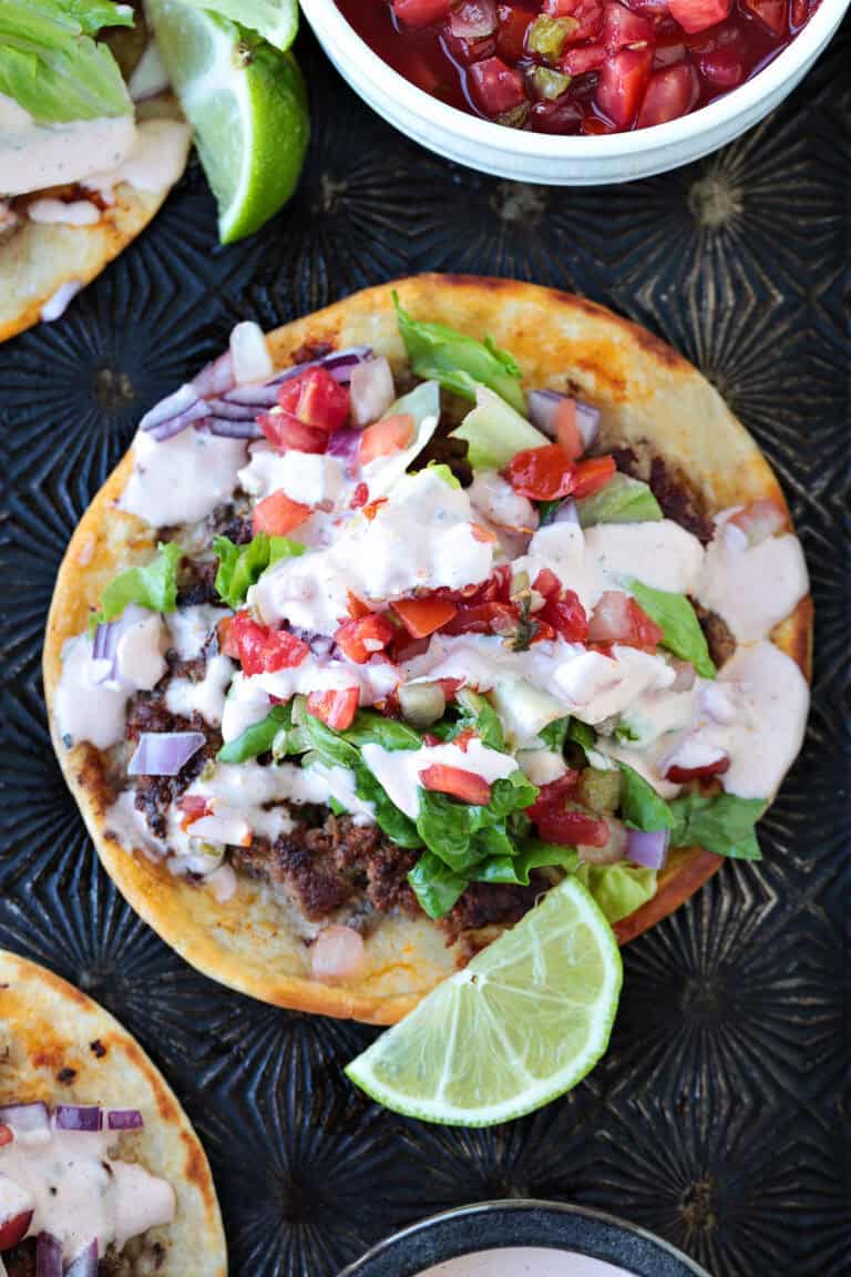 smash taco with toppings and sauce and limes on the side