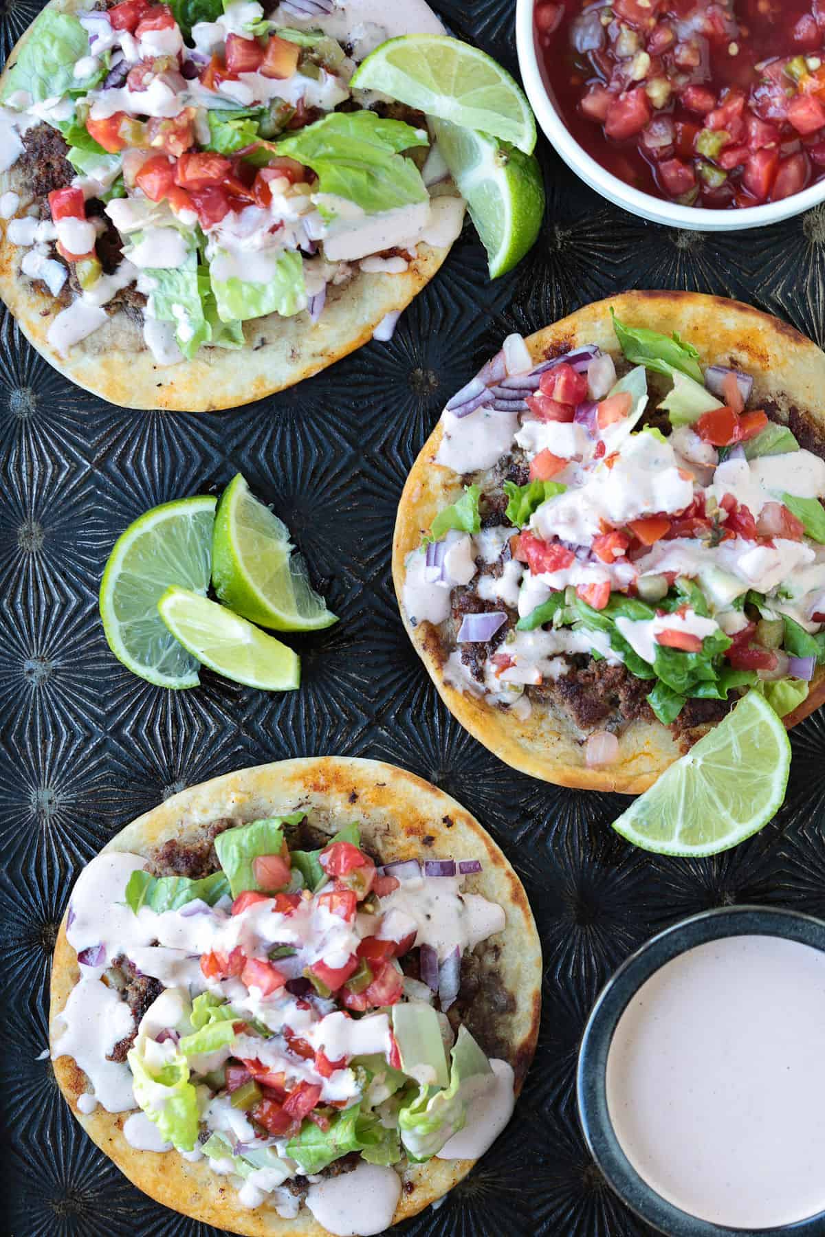 Smash Tacos are the key to fun dinners that everyone loves. Seasoned ground beef cooked on a crispy tortilla with your favorite toppings! open face tacos on a sheet pan with toppings and sauce