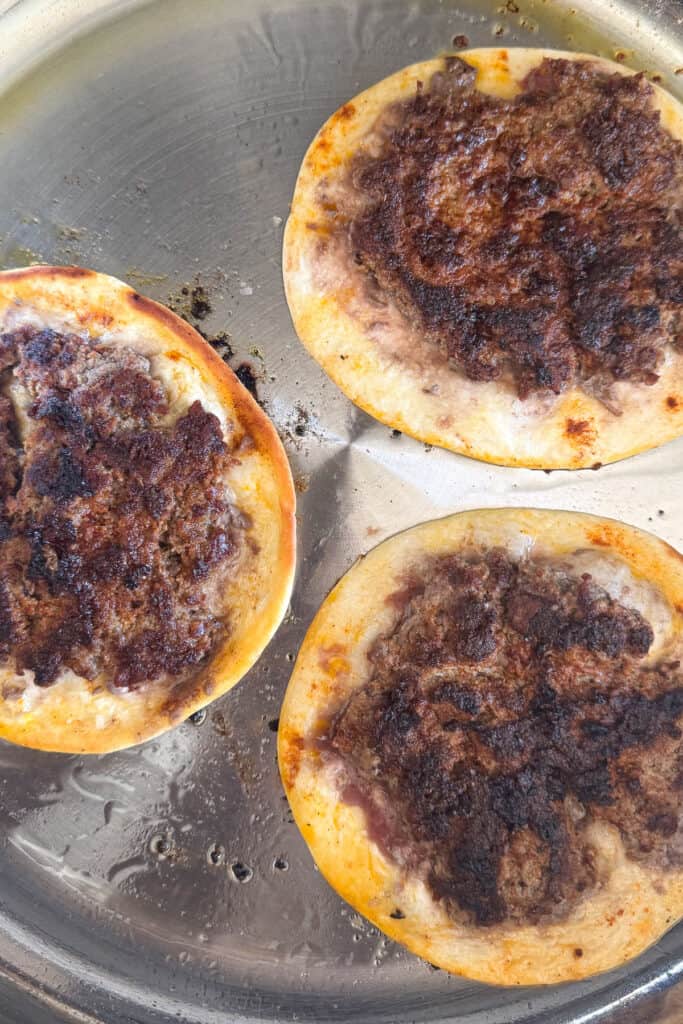 Smash Tacos are the key to fun dinners that everyone loves. Seasoned ground beef cooked on a crispy tortilla with your favorite toppings! cooked ground beef on tortillas in skillet