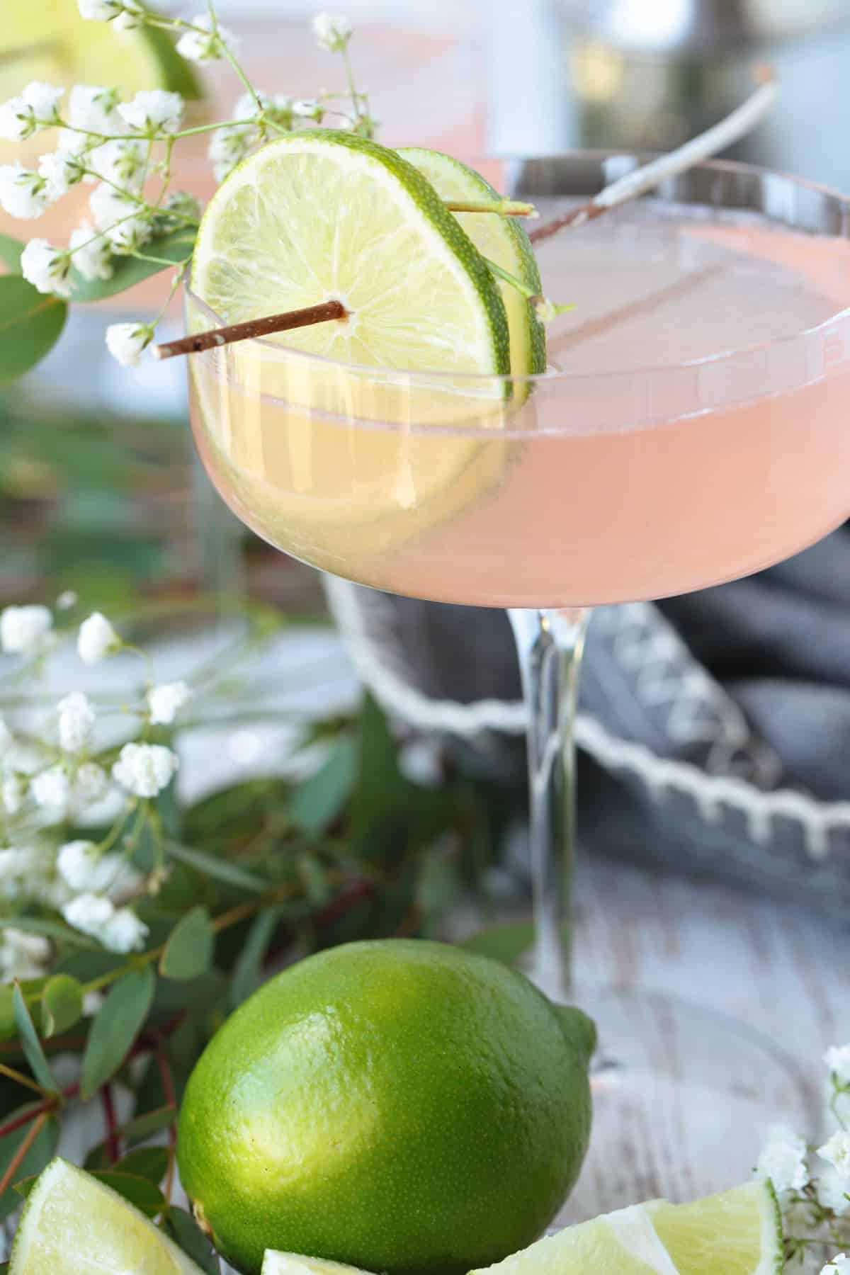 cosmopolitan cocktail with limes and floral garnish