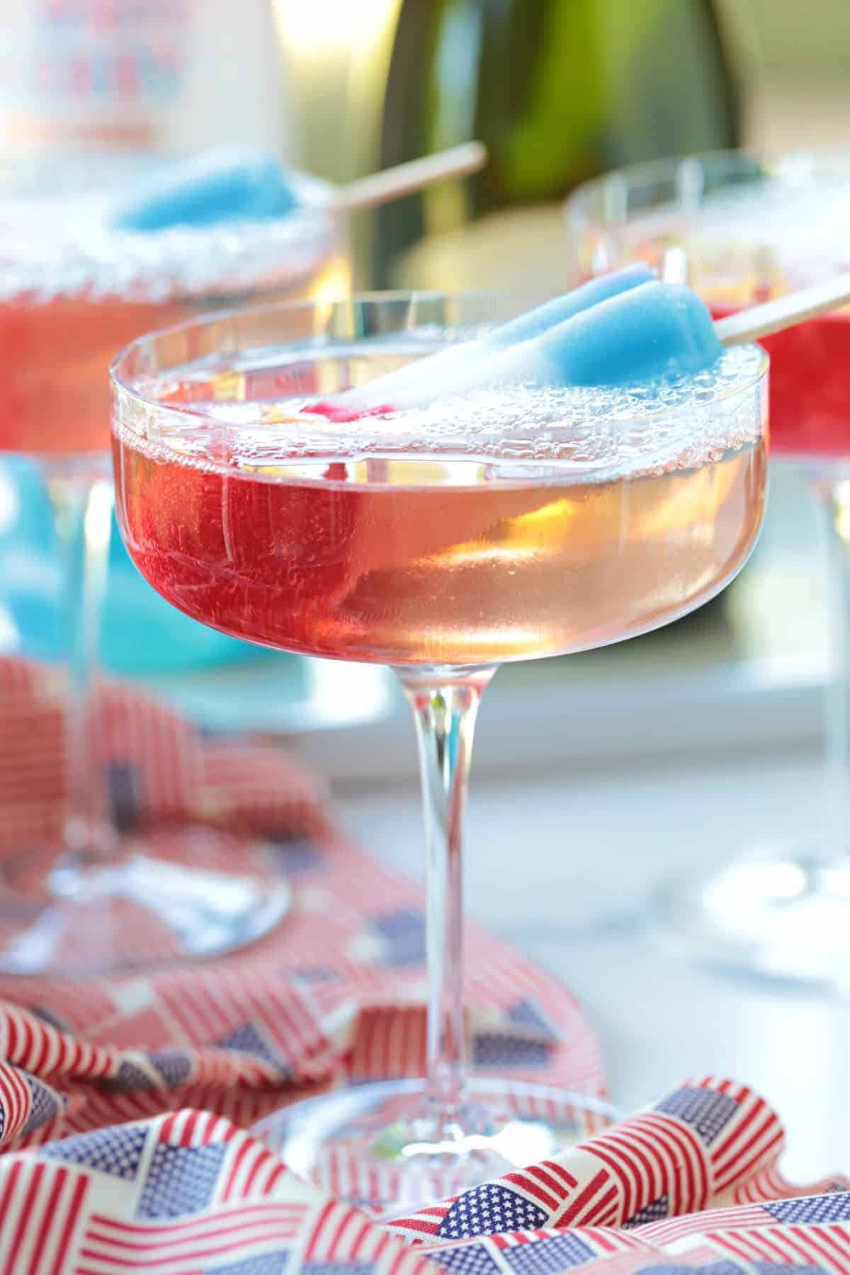 This Bomb Pop Cocktail is the easiest summer drink you'll ever make! The popsicle melts into the champagne for added fun and flavor! bomb pop cocktail with flag tablecloth