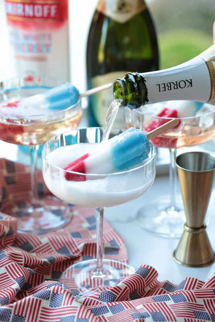 This Bomb Pop Cocktail is the easiest summer drink you'll ever make! The popsicle melts into the champagne for added fun and flavor! champagne being poured into champagne glass with ice pop