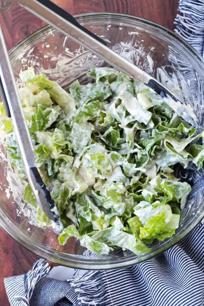 shredded lettuce in a glass bowl with caesar dressing