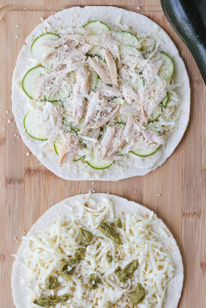 Crispy Chicken Zucchini Quesadillas are filled with tender chicken, thinly sliced zucchini and gooey cheese for an easy 30 minute dinner. tortillas with cheese, chicken and sliced zucchini on a board