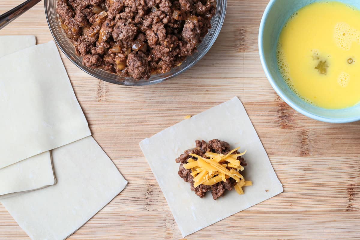 Cheeseburger Wontons are sure to become a new favorite! A beefy, cheesy filling stuffed into crispy wontons and dipped in our big mac sauce! open wonton with ground beef and cheese filling, bowl of ground beef on the side along with bowl of egg wash