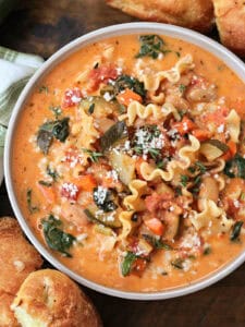 bowl of minestrone soup in a creamy broth with rolls on the side