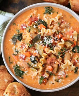 bowl of minestrone soup in a creamy broth with rolls on the side