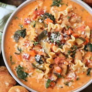 bowl of minestrone soup in a creamy broth with rolls on the side