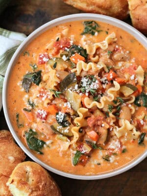 bowl of minestrone soup in a creamy broth with rolls on the side