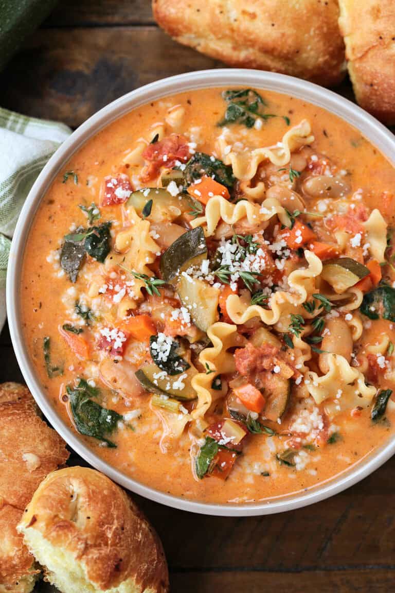 bowl of minestrone soup in a creamy broth with rolls on the side