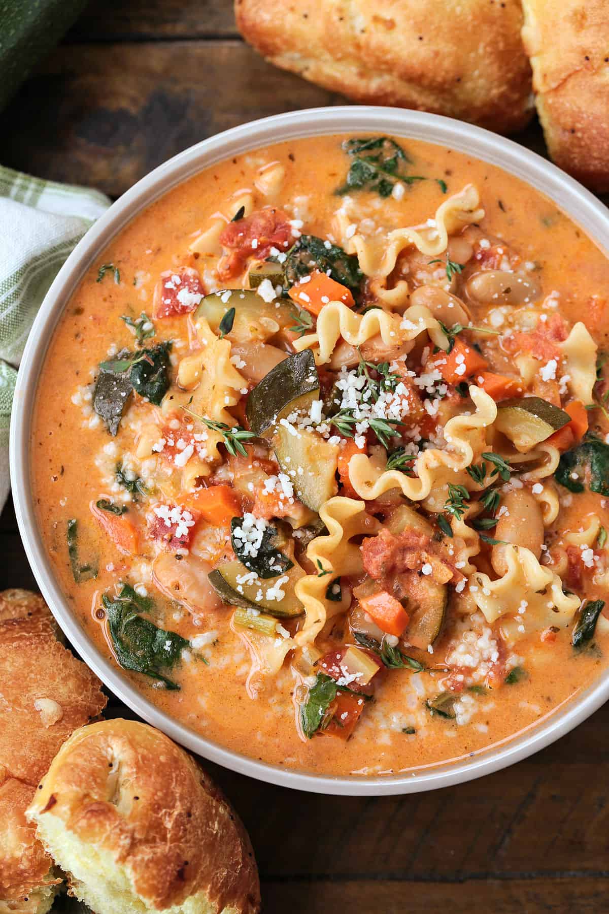 bowl of minestrone soup in a creamy broth with rolls on the side