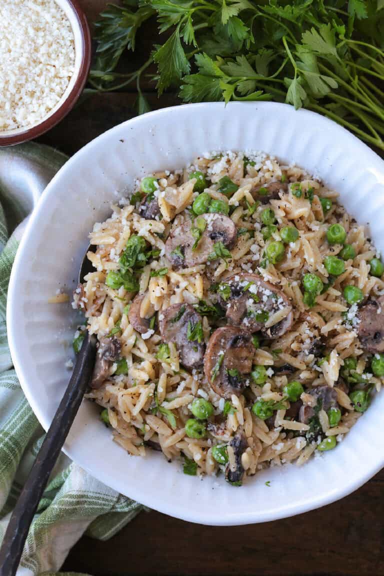 orzo with mushrooms and peas in a white bowl with spoon