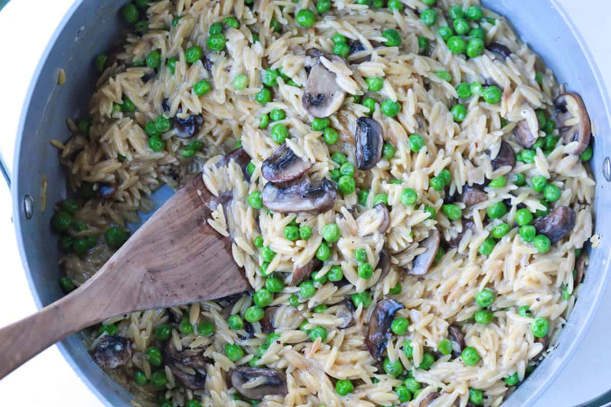 This Creamy Mushroom Orzo with Peas is made with tender pasta, savory mushrooms and sweet peas in a rich, creamy sauce. An easy side dish or a meatless dinner! mushroom and pea orzo in a pot with wooden spoon