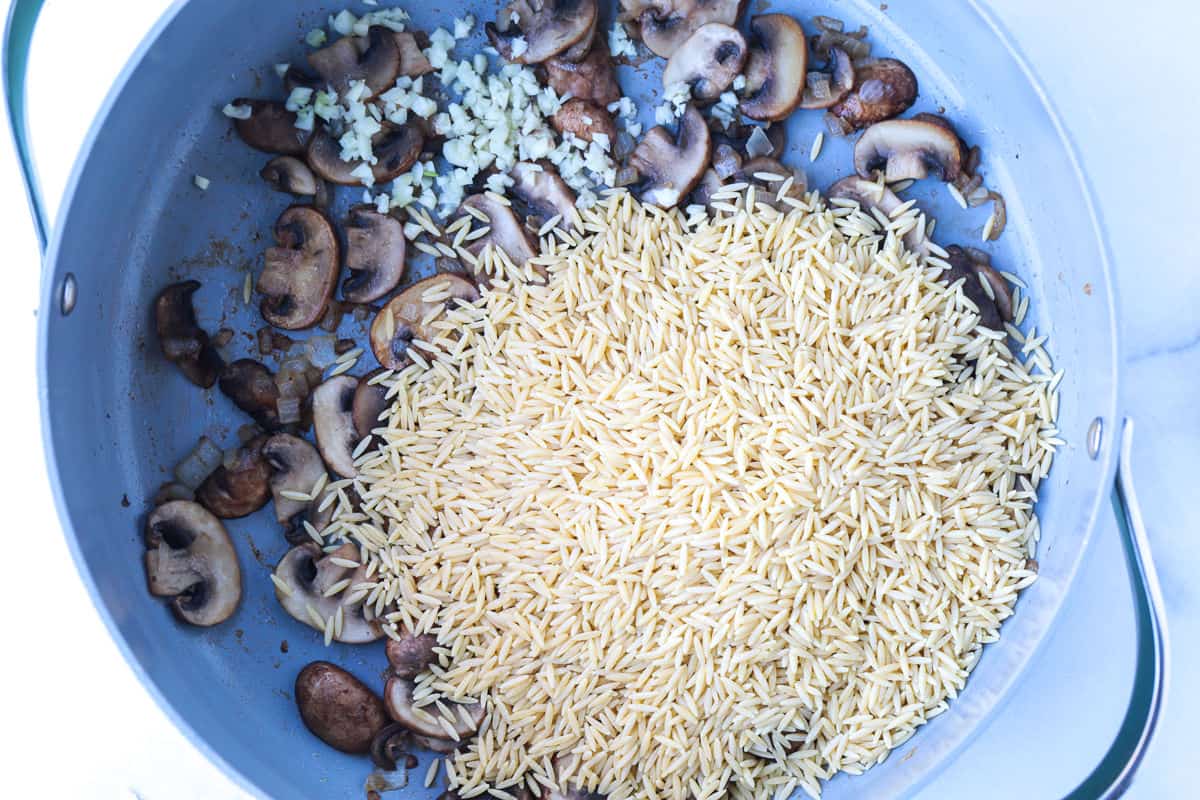 This Creamy Mushroom Orzo with Peas is made with tender pasta, savory mushrooms and sweet peas in a rich, creamy sauce. An easy side dish or a meatless dinner! browned mushrooms in a pot with onions and dry orzo