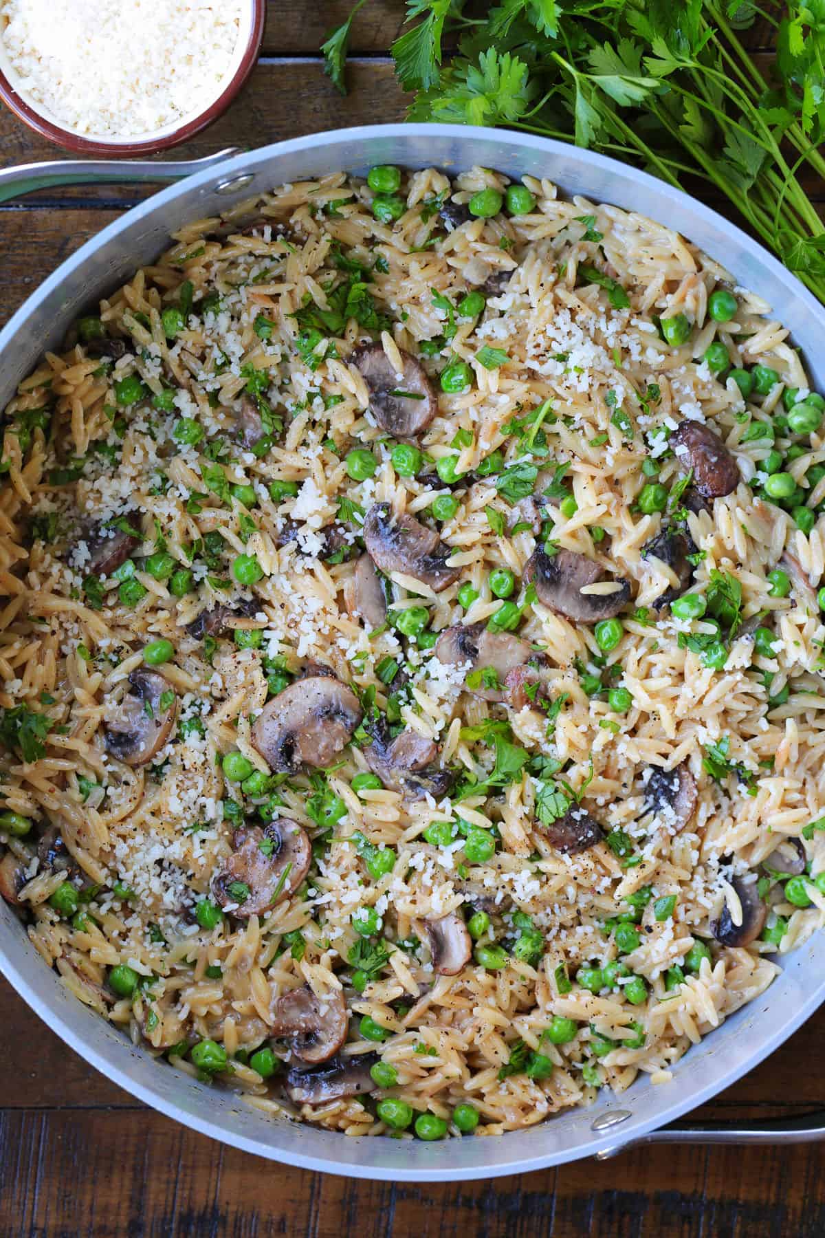 This Creamy Mushroom Orzo with Peas is made with tender pasta, savory mushrooms and sweet peas in a rich, creamy sauce. An easy side dish or a meatless dinner! mushroom and pea orzo in a pot with parmesan cheese and parsley on the side